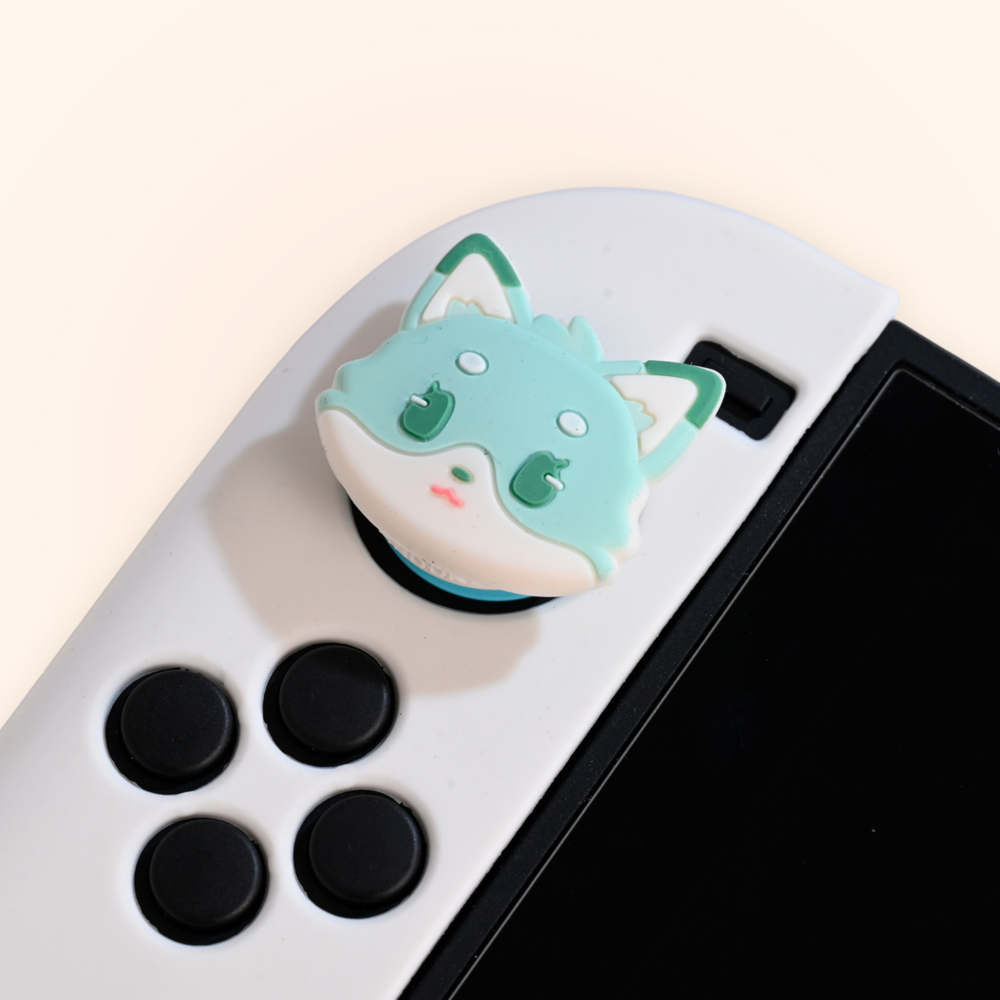 Una cubierta de joystick con forma de zorro turquesa en un mando de juego blanco. Se ven botones negros. La pantalla es negra.