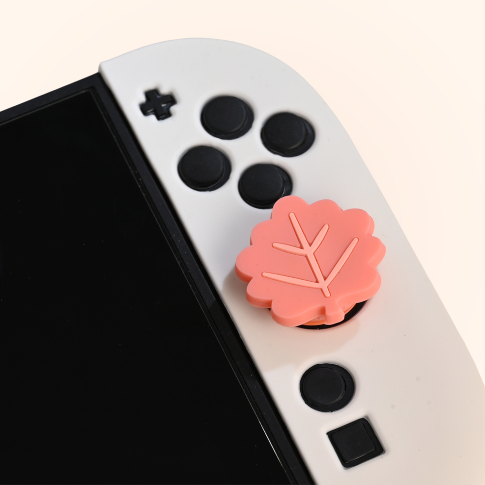 Un mando de juego blanco con botones negros y una empuñadura para el pulgar en forma de hoja rosa está encima de la pantalla.