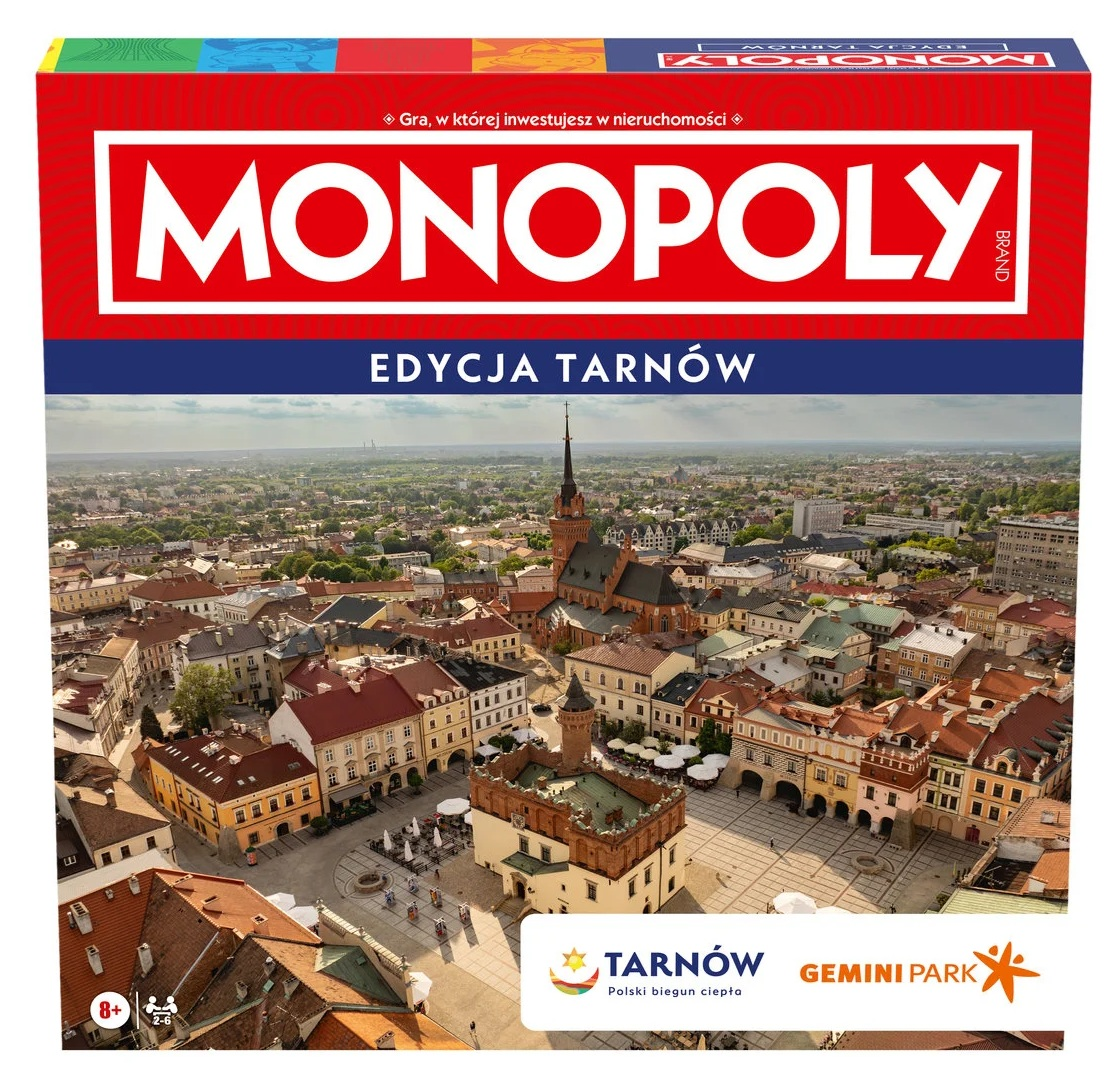 Pudełko gry planszowej Monopoly, edycja Tarnów, z widokiem na miasto z kościołem i rynkiem. Dominują kolory czerwony, biały i niebieski.