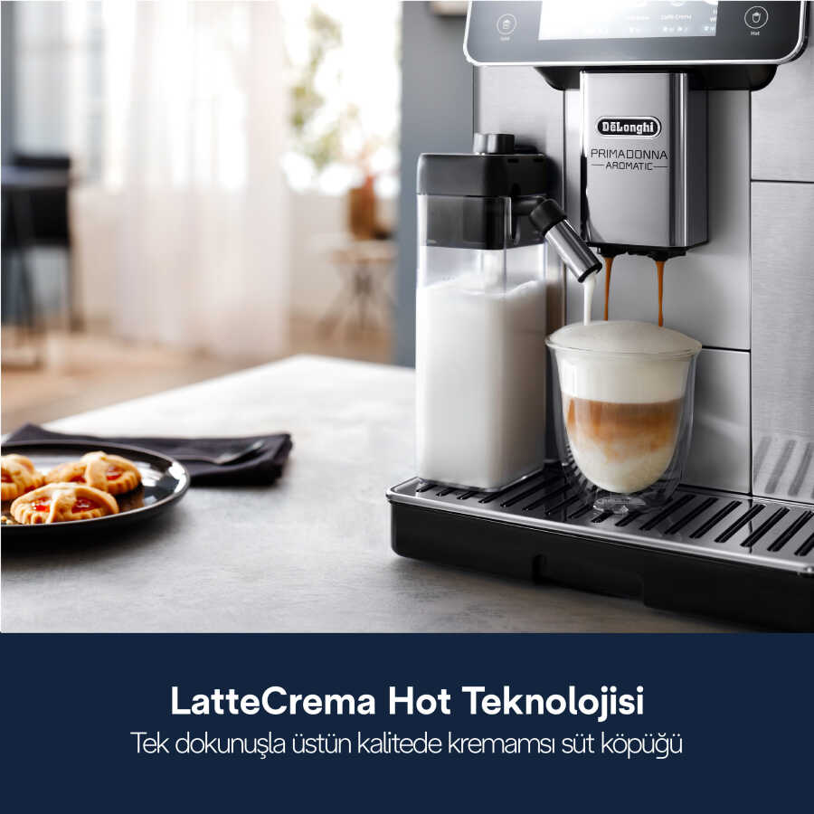 Bir kahve makinesi, bir bardağa katmanlı latte dağıtıyor. Süt kabı solda, kurabiyeler sağda bir tabakta.