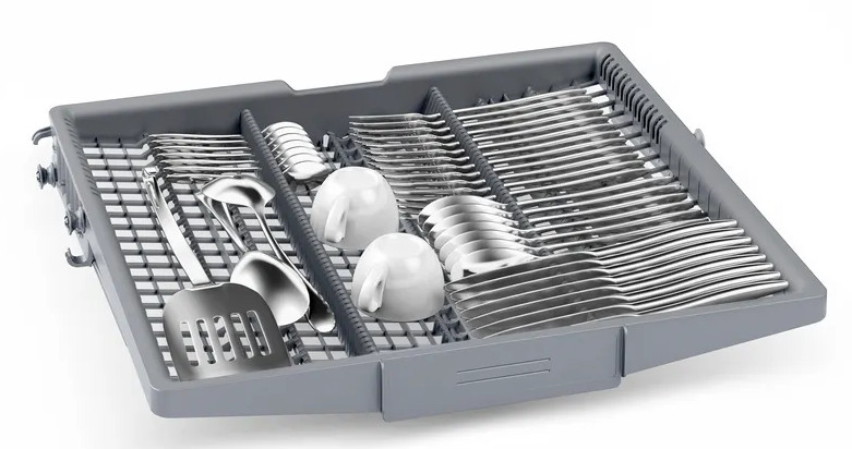 Taca zmywarki wypełniona sztućcami, dwoma filiżankami i przyborami do serwowania. Taca jest szara na białym tle.