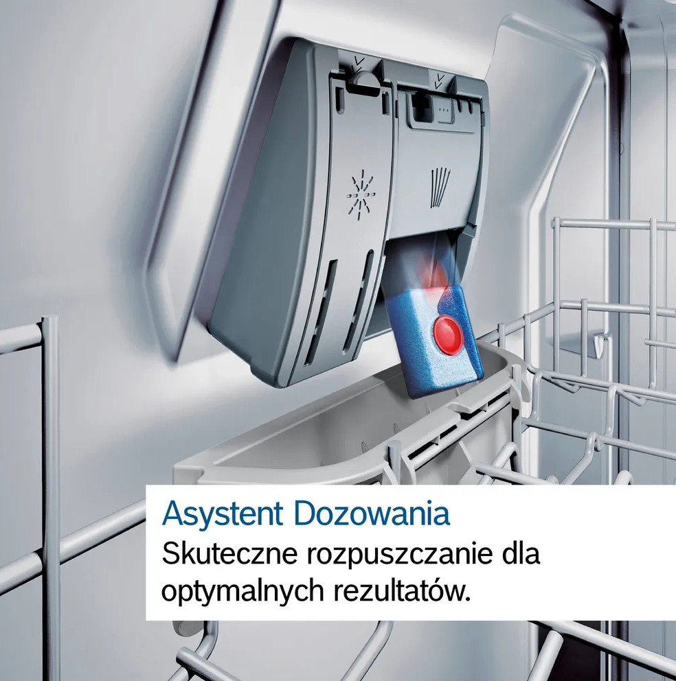 Dozownik do detergentów do zmywarki. Niebieska tabletka z czerwonym środkiem znajduje się w dozowniku. Dozownik jest szary, wnętrze zmywarki białe.