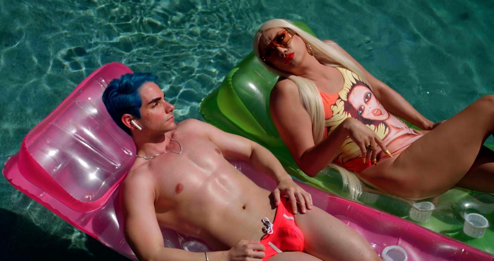Zwei Personen auf Schwimmmatratzen in einem Pool. Einer hat blaues Haar und der andere trägt einen Badeanzug.