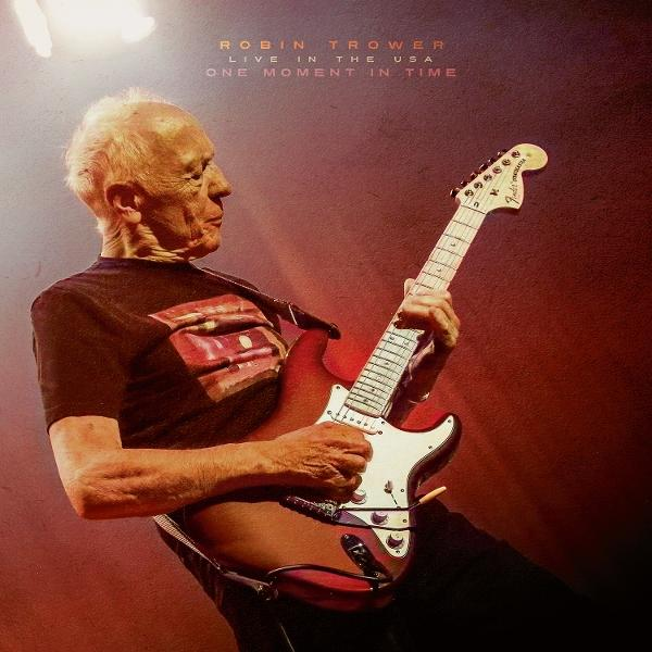 Älterer Mann spielt rote E-Gitarre. Er trägt ein schwarzes Hemd mit Design. Der Hintergrund ist dunkelrot.