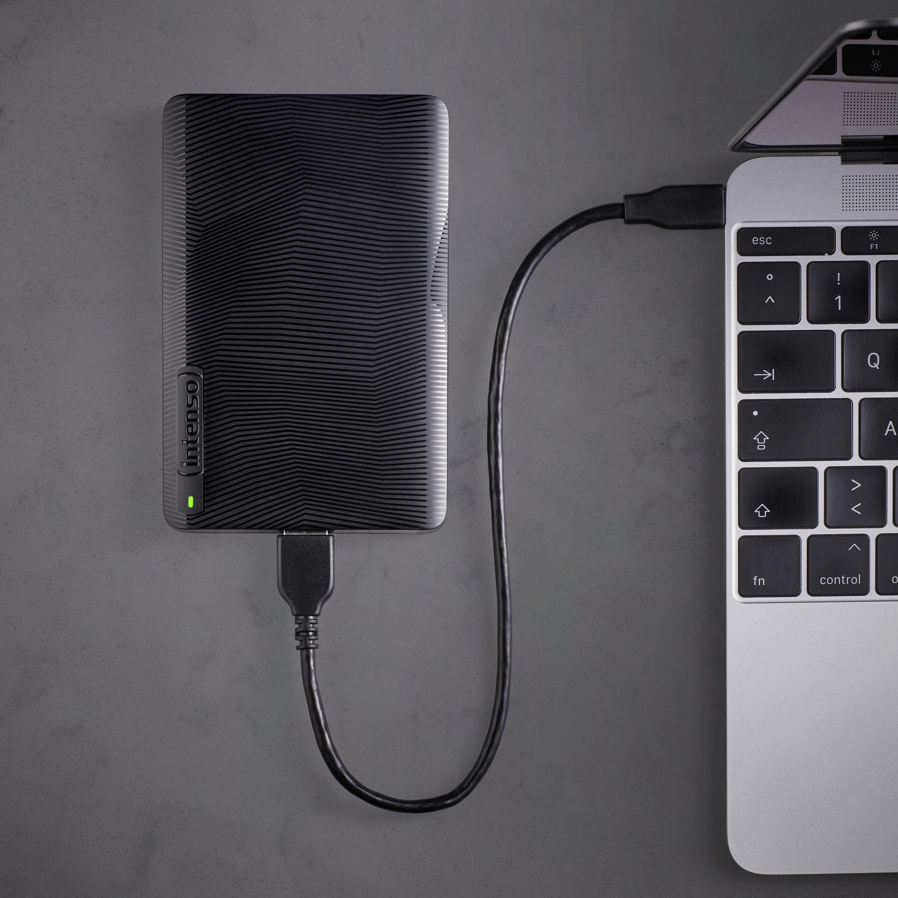 Eine schwarze externe Festplatte, die über ein USB-Kabel mit einem Laptop verbunden ist, auf einer grauen Oberfläche.