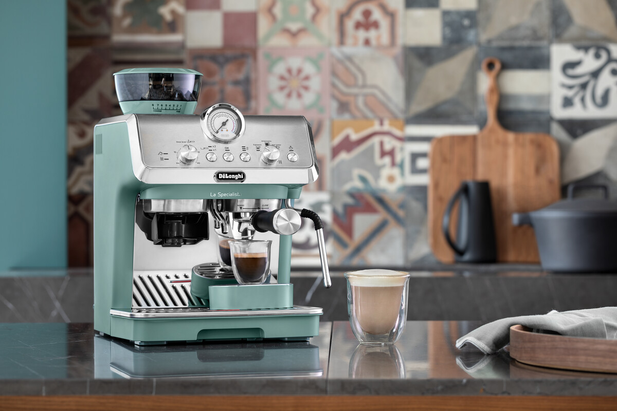 Egy eszpresszó gép egy csésze kávéval és egy latte-val. Fa vágódeszka, fekete bögre és edény a háttérben.