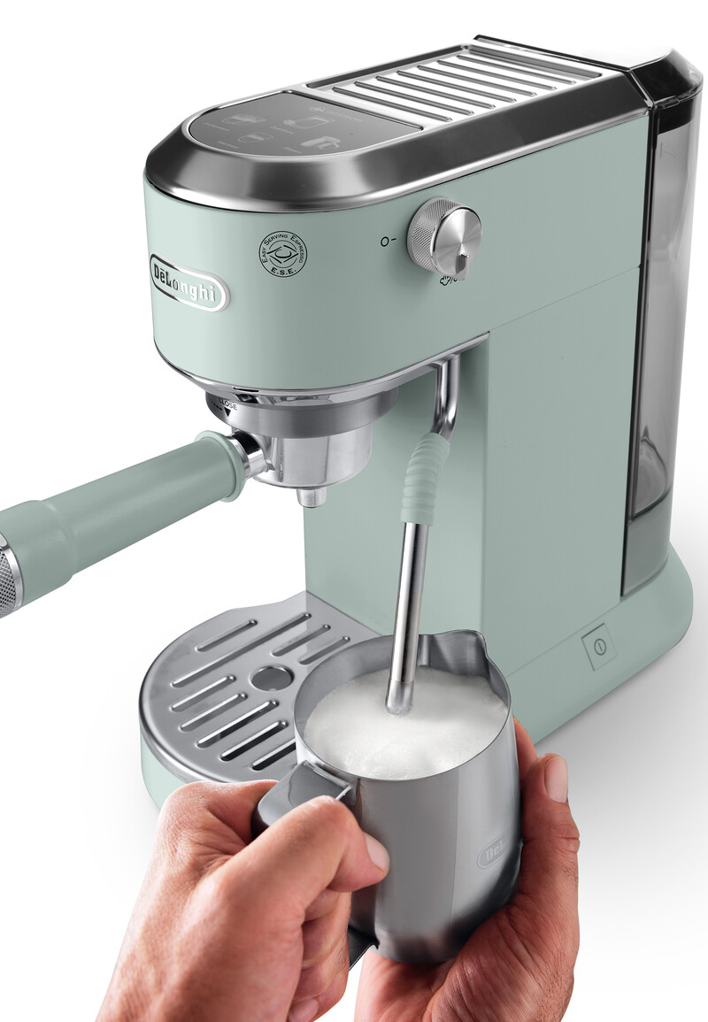 Mentazöld DeLonghi eszpresszógép. Egy kéz egy tejhabosító kancsót tart habosított tejjel.