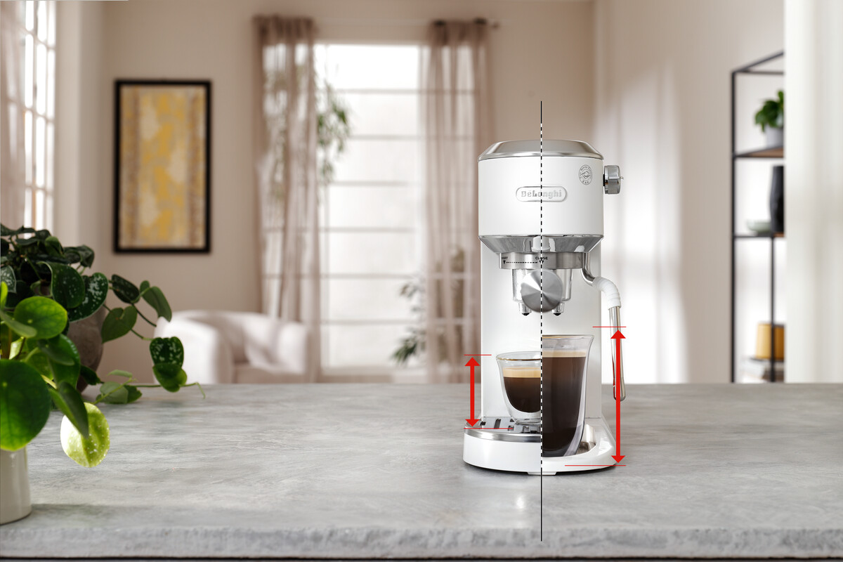 Fehér Delonghi eszpresszógép egy kávéval teli pohárral. A háttérben egy növény és egy festmény.