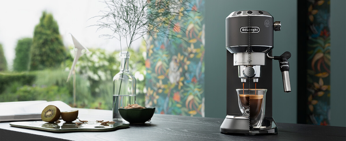 Espresszógép, amint kávé ömlik egy pohárba. Kiwi és üvegváza növényekkel a háttérben. Színes függöny.