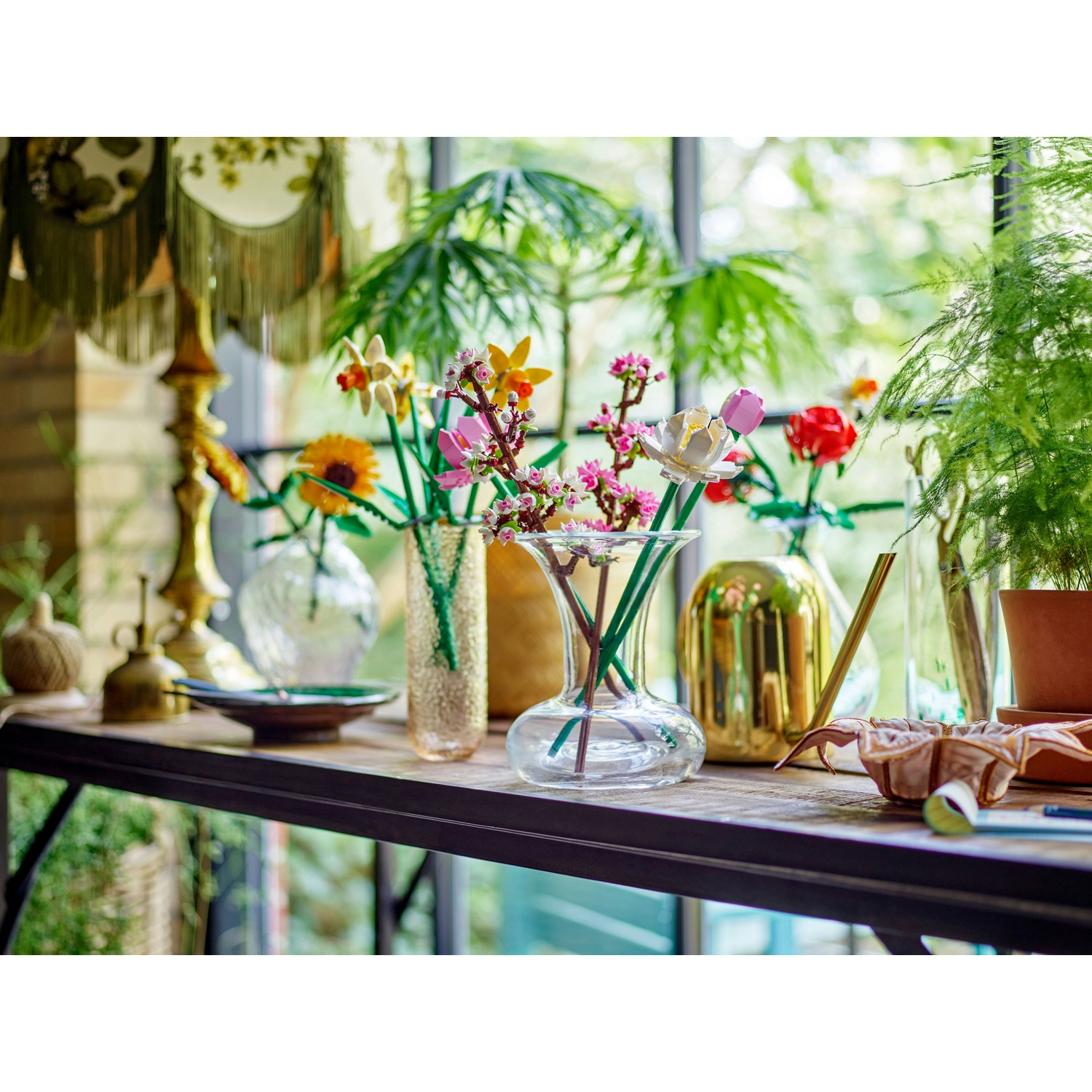 Una mensola espone vari vasi con fiori colorati. Una lampada e piante sullo sfondo, con vista finestra dietro.