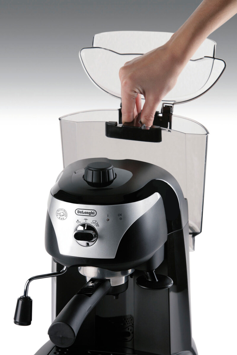 Egy kéz felemeli egy fekete-ezüst DeLonghi eszpresszógép fedelét. A víztartály látható.