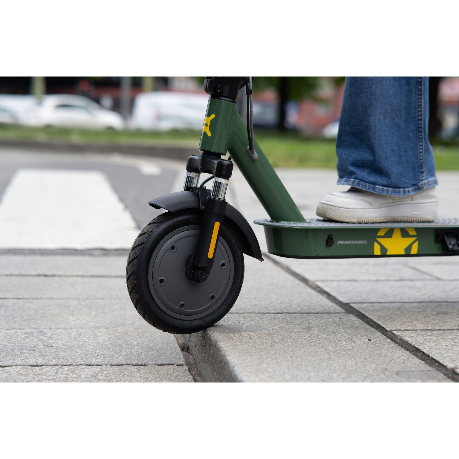 A person on a green scooter. The scooter has a black tire and a yellow star. The person wears jeans and white shoes.