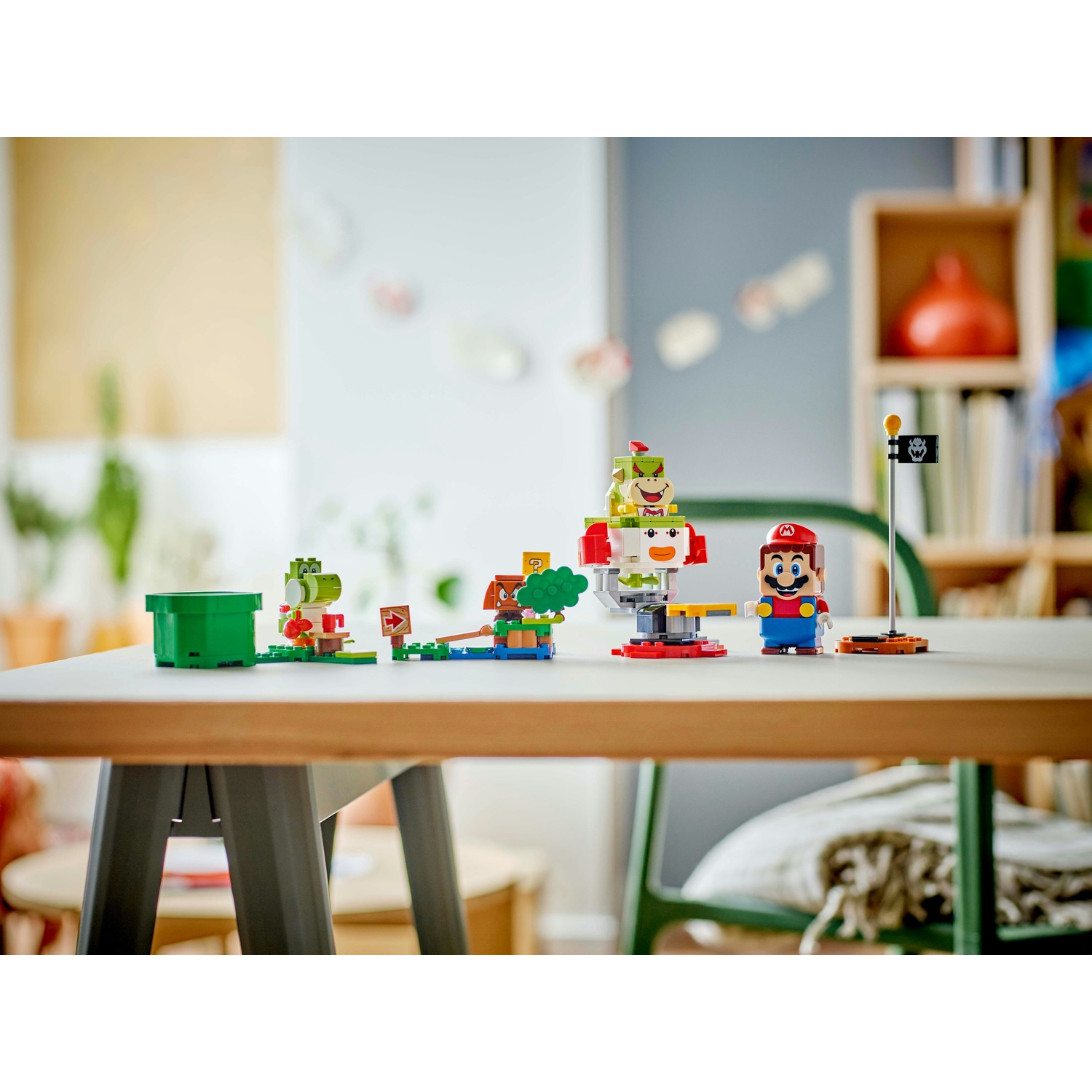 Set Lego di Mario su un tavolo bianco. Include Mario, Bowser Jr., una bandiera e altre figure Lego. Lo sfondo è un'ambientazione in una stanza.
