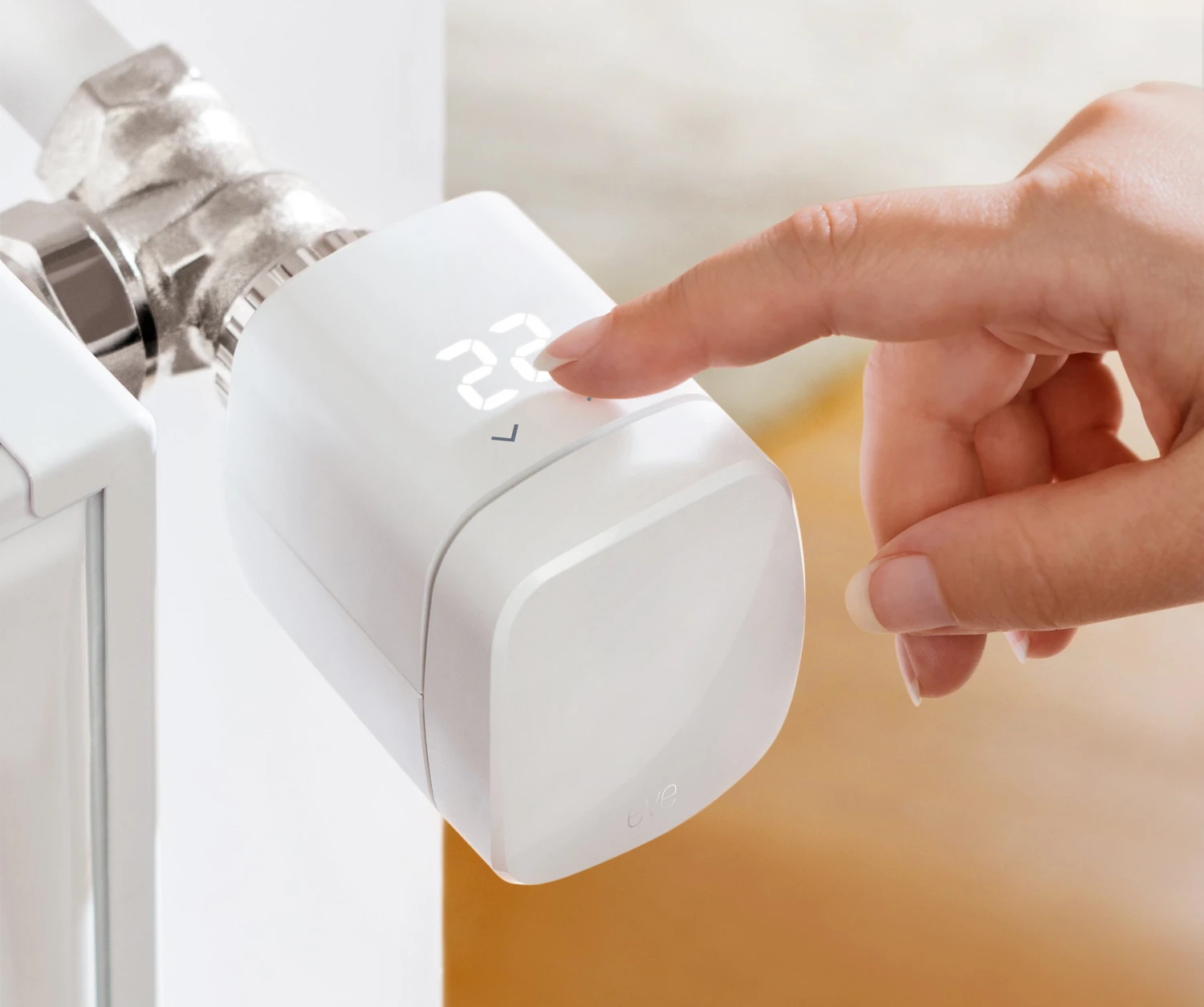 Eine Hand drückt auf ein weißes Thermostat, das 22 anzeigt. Das Thermostat ist an ein Rohr angeschlossen. Der Hintergrund ist unscharf.