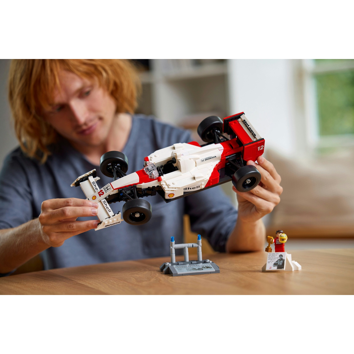 Una persona che tiene in mano una macchina da corsa Lego. L'auto è bianca e rossa. Ci sono altri pezzi Lego sul tavolo.