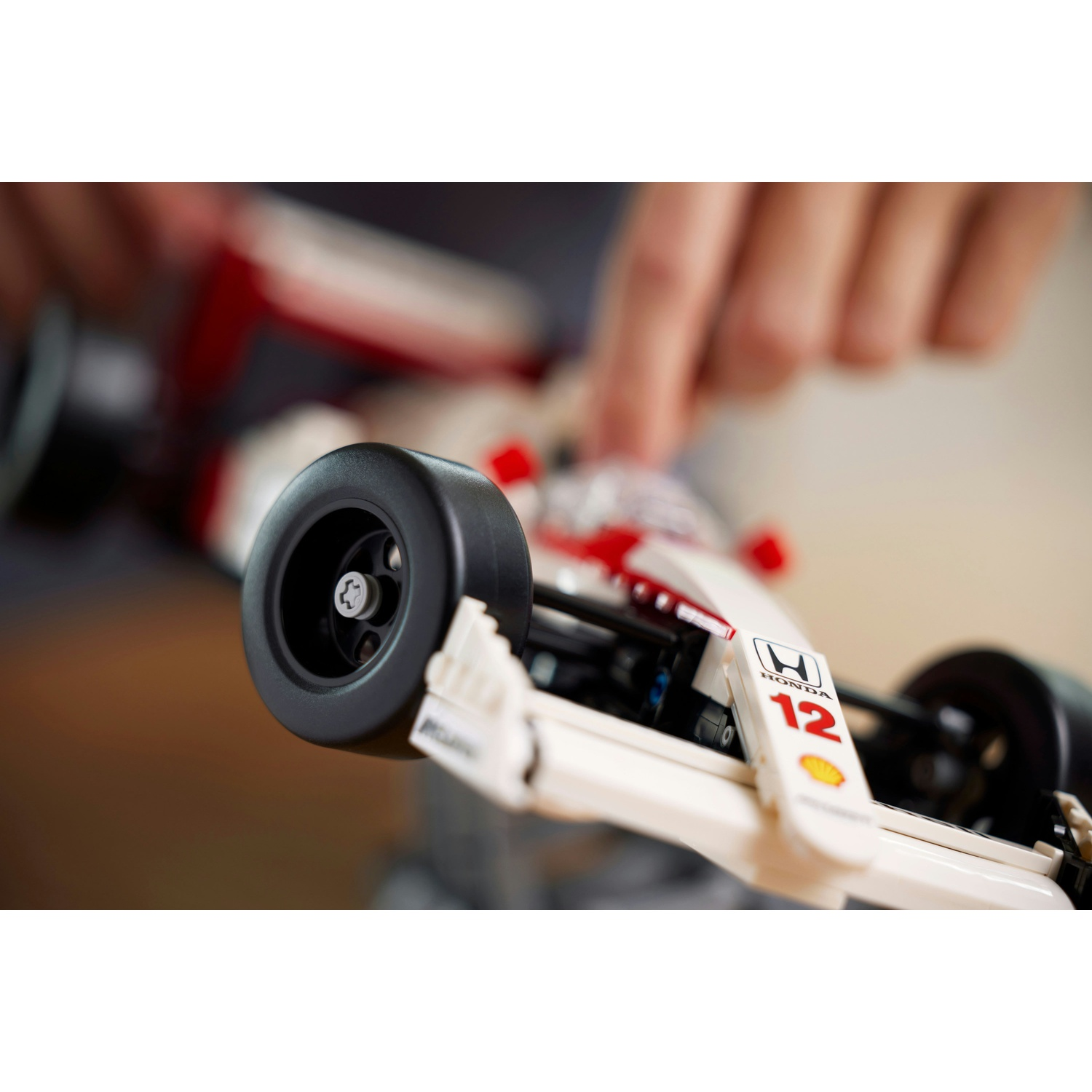 Primo piano di una macchina da corsa Lego. L'auto è bianca e rossa, con un pneumatico nero in primo piano e le mani sullo sfondo.