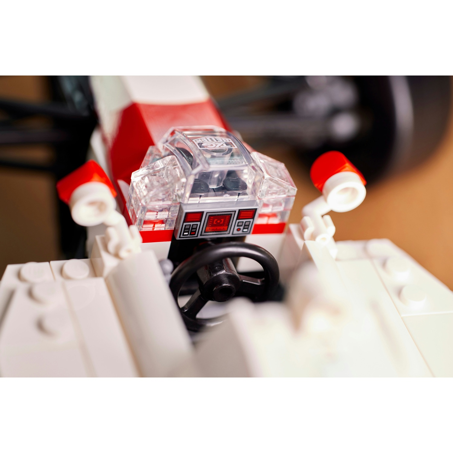 Un abitacolo di una macchina da corsa Lego. È dotato di una cupola trasparente, dettagli rossi e bianchi, un volante nero e una luce rossa.