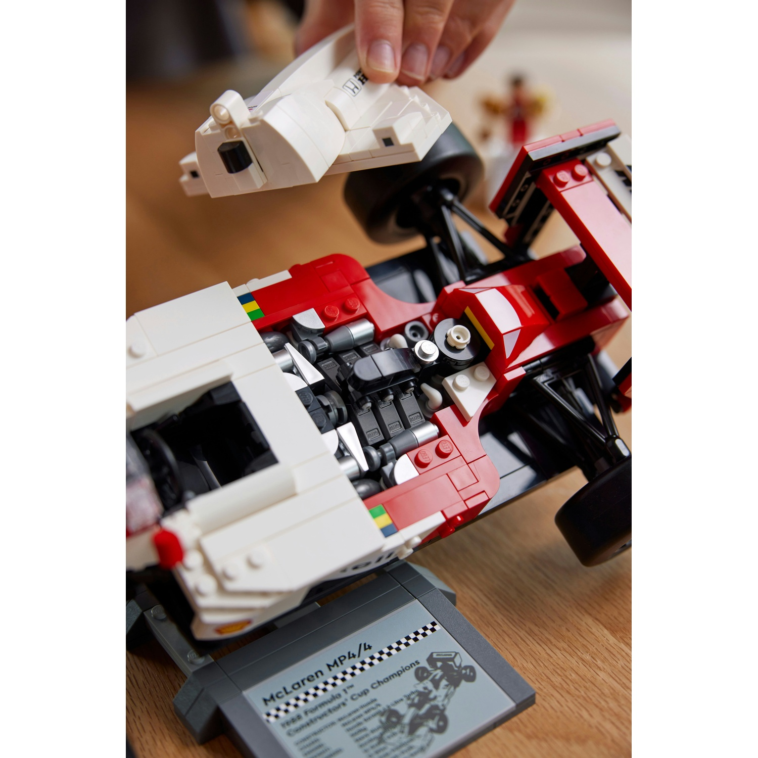 Una persona sta assemblando un'auto da corsa Lego rossa e bianca. L'auto è parzialmente costruita, con una base grigia e una parte bianca che viene aggiunta.