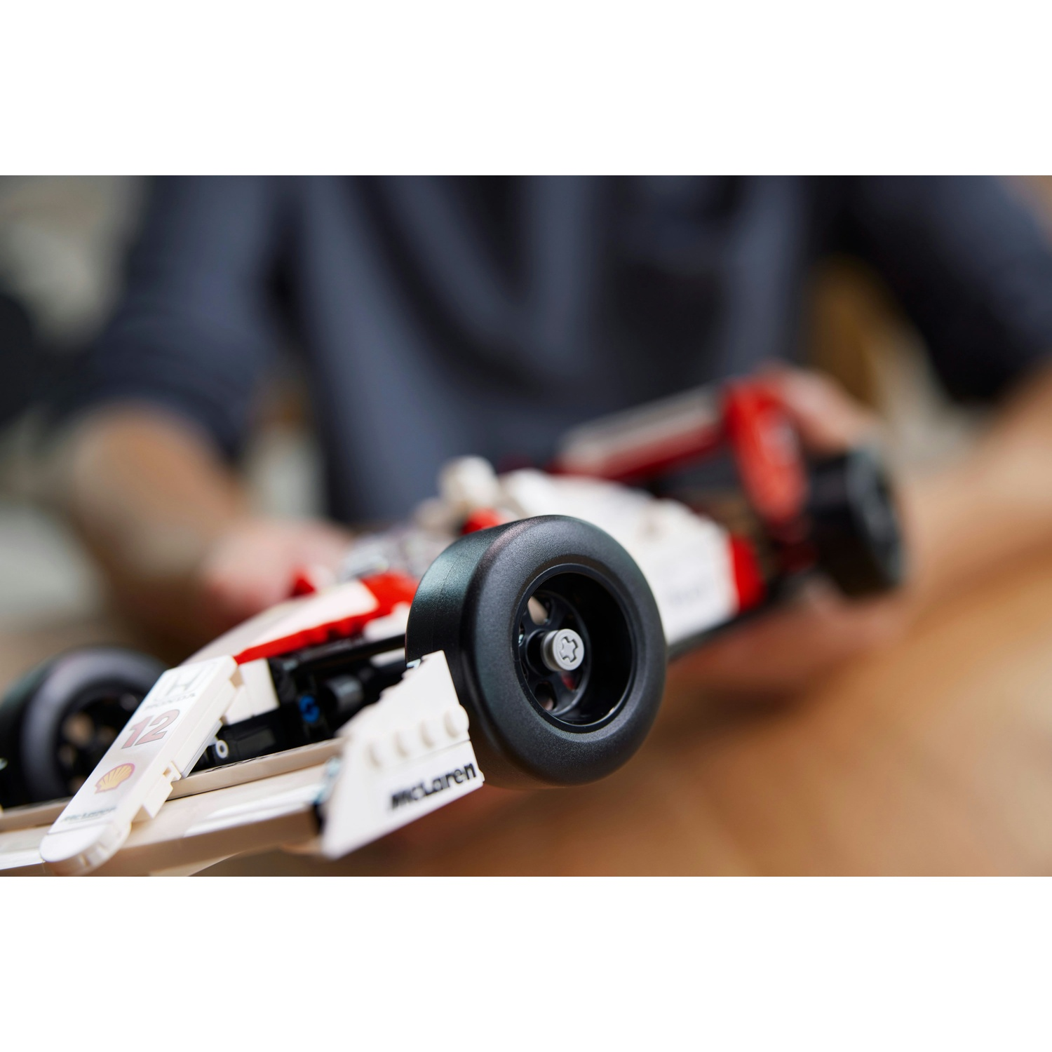 Un'auto da corsa Lego è tenuta da una persona. L'auto è bianca, rossa e nera. Ha il logo McLaren e il numero 12.