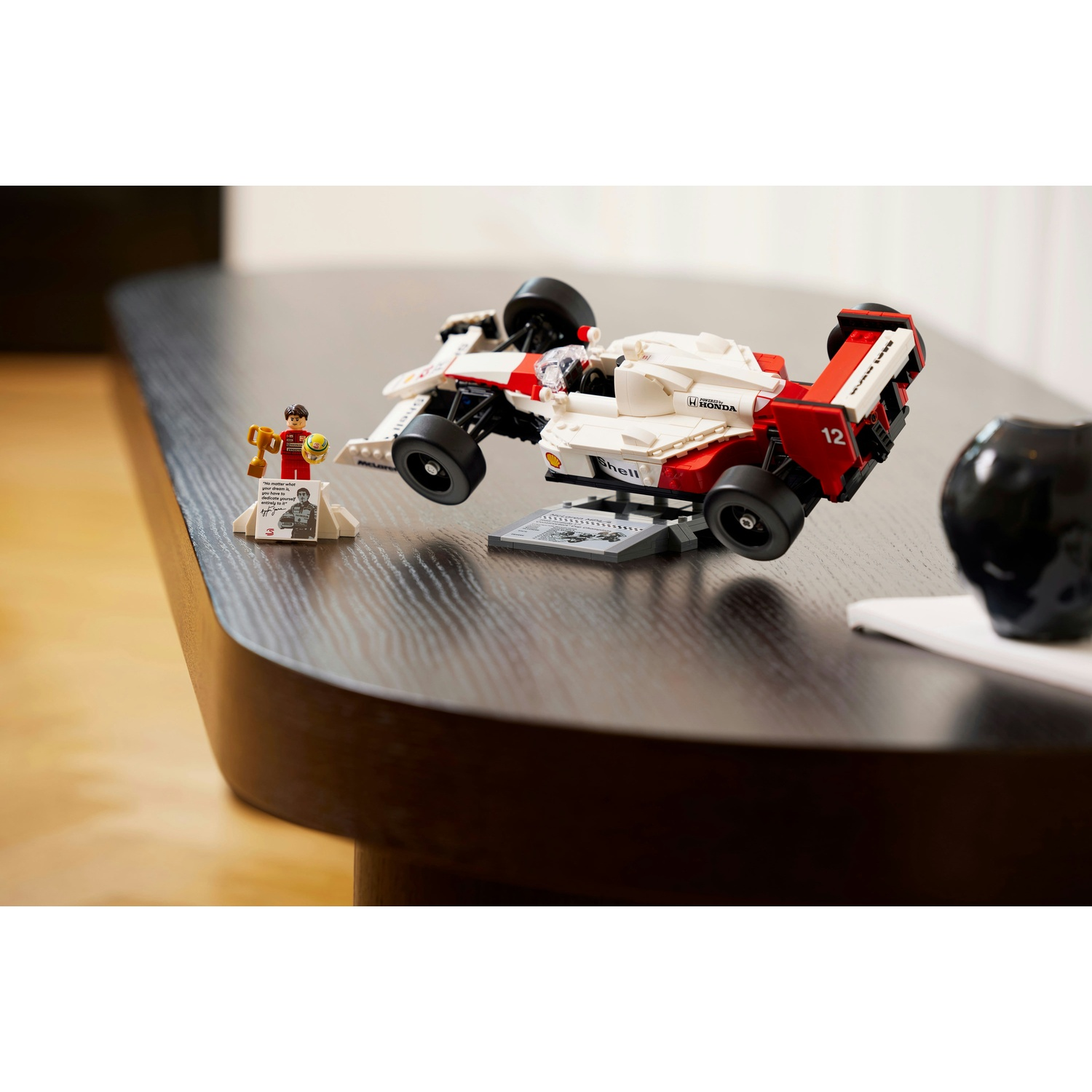 Auto F1 Lego con una figura di pilota e un trofeo su un tavolo. L'auto è bianca e rossa, la figura tiene un trofeo.