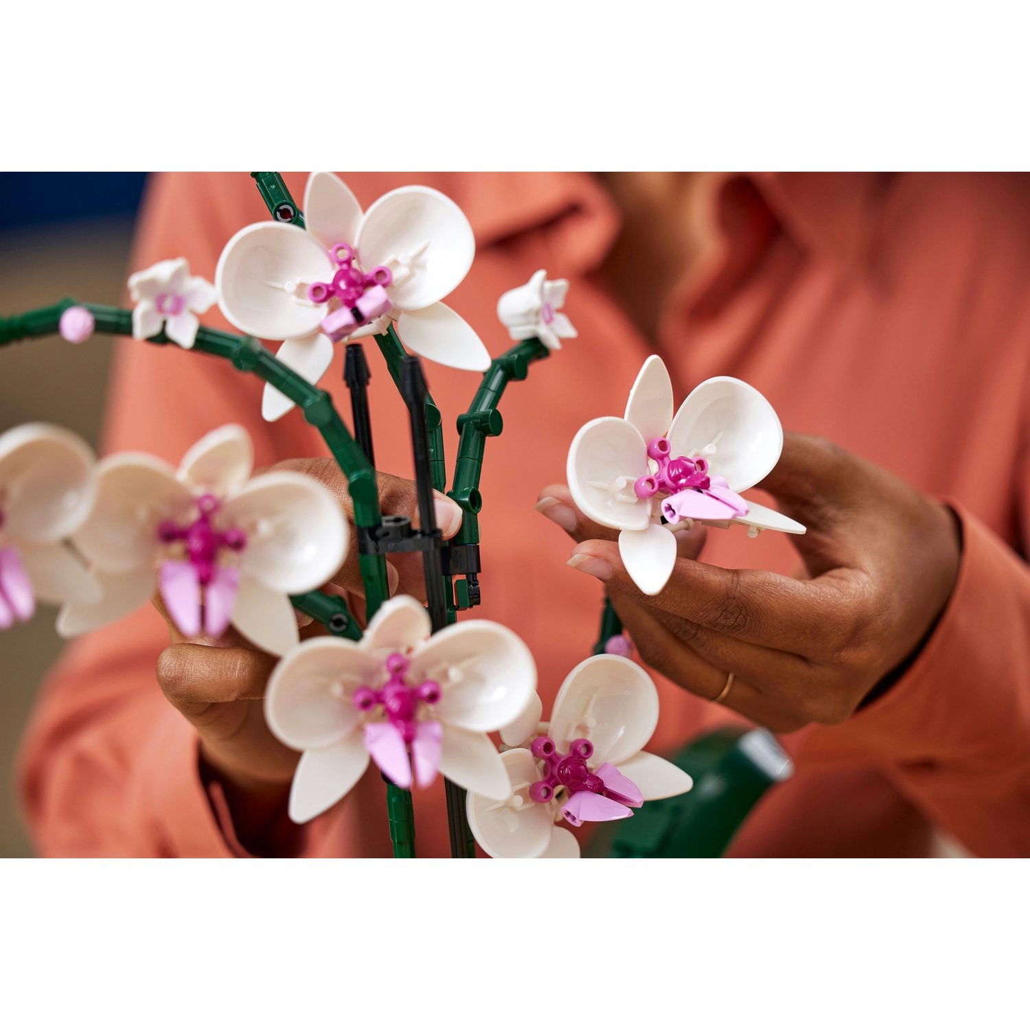 Mani che tengono un'orchidea Lego bianca e rosa, con una camicia color corallo sullo sfondo.