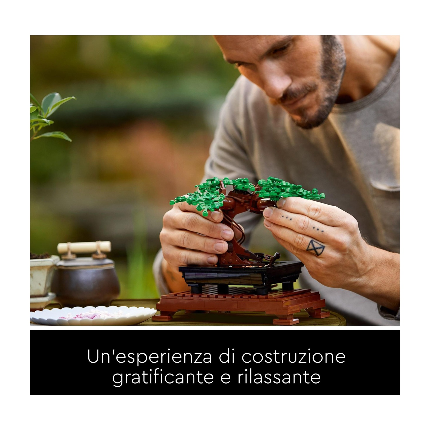 Un uomo costruisce un modello di albero bonsai. È marrone con foglie verdi. Altre piante e vasi sono sullo sfondo.