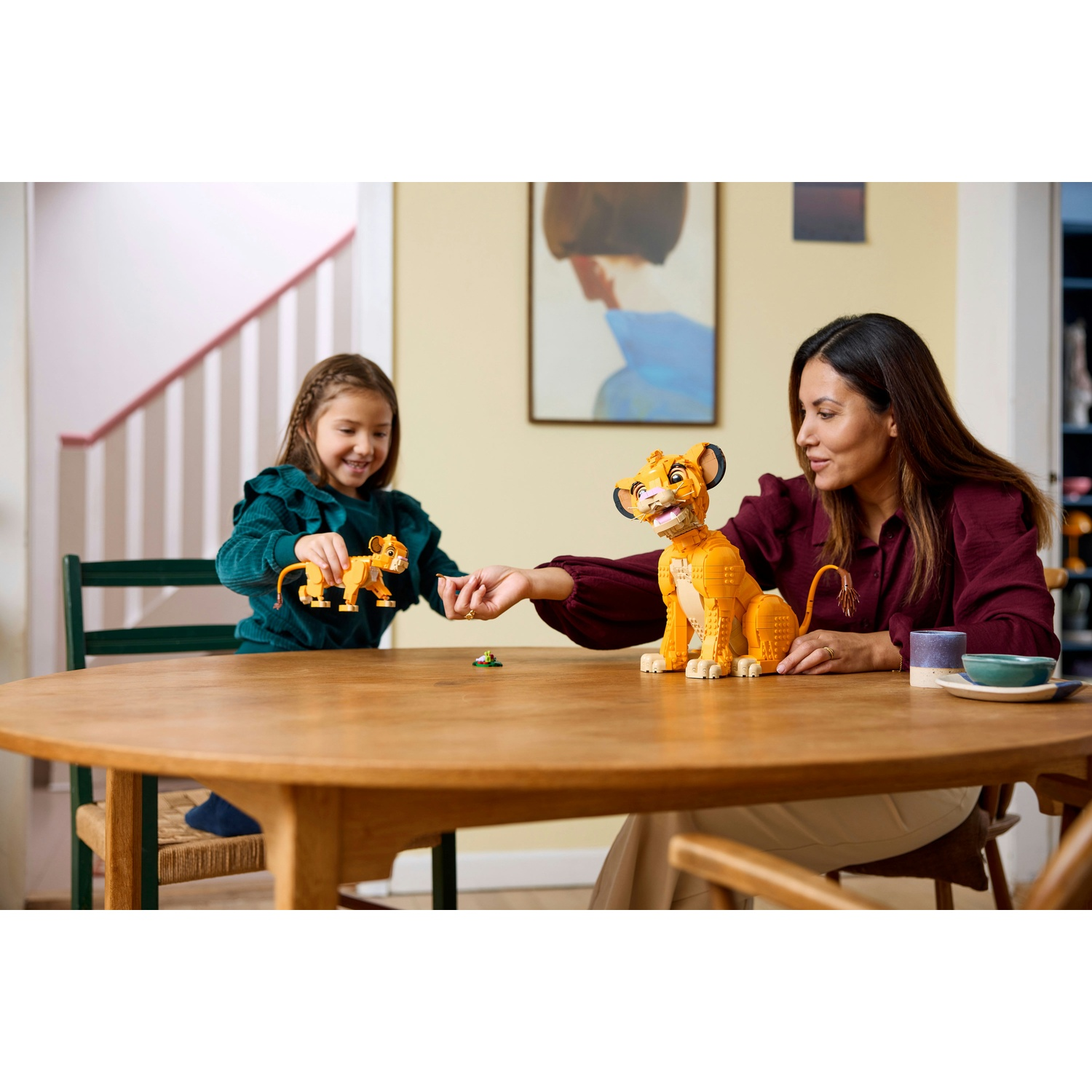 Una donna e una bambina giocano con i giocattoli Lego Simba su un tavolo di legno. La donna indossa una camicia bordeaux, la bambina una verde.