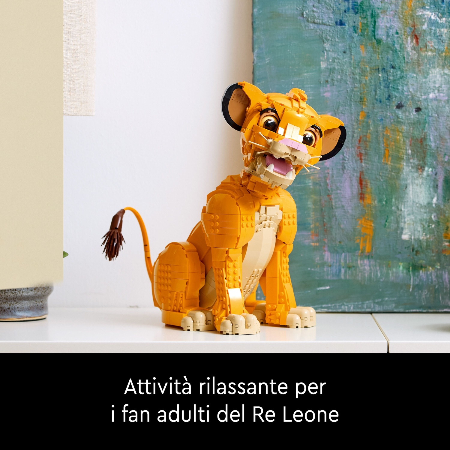 Un modello Lego di Simba è su una mensola bianca. Il modello è arancione e beige. Un dipinto è sullo sfondo.