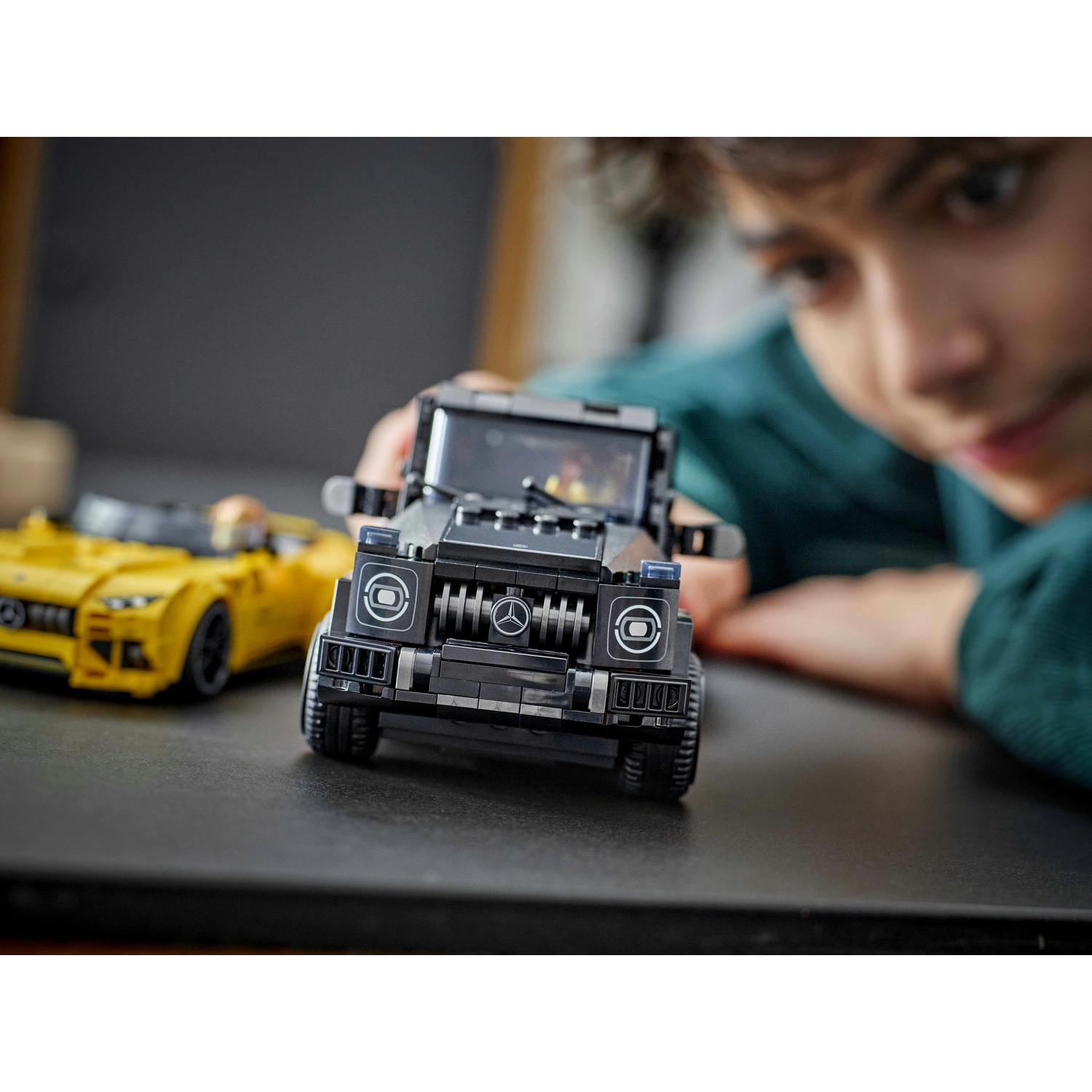 Un bambino tiene in mano una macchina Lego nera, con una macchina Lego gialla sullo sfondo. Il bambino guarda la macchina nera.