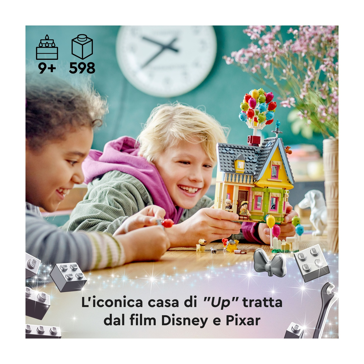 Due bambini costruiscono una casa Lego del film "Up". La casa è gialla con palloncini. Lo sfondo include fiori.