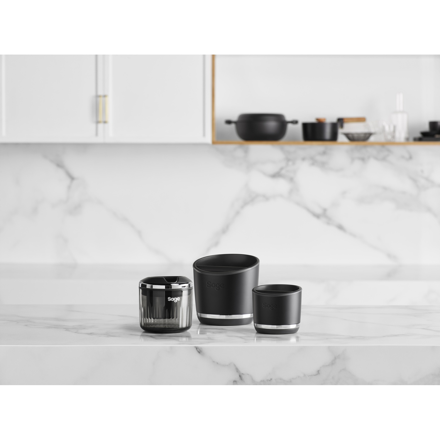 Three black Sage containers on a marble counter. Background: white cabinets and shelves with black cookware.