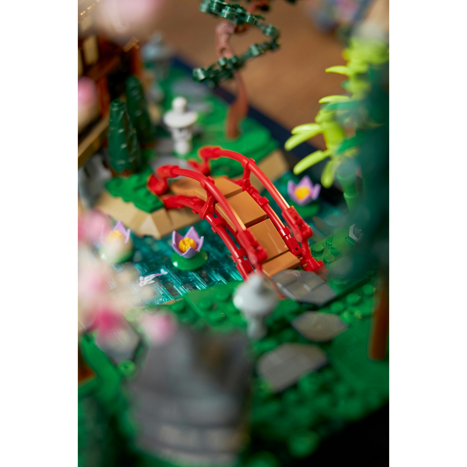 Una scena in miniatura con un ponte rosso su uno stagno con ninfee e una casa e alberi in miniatura sullo sfondo.