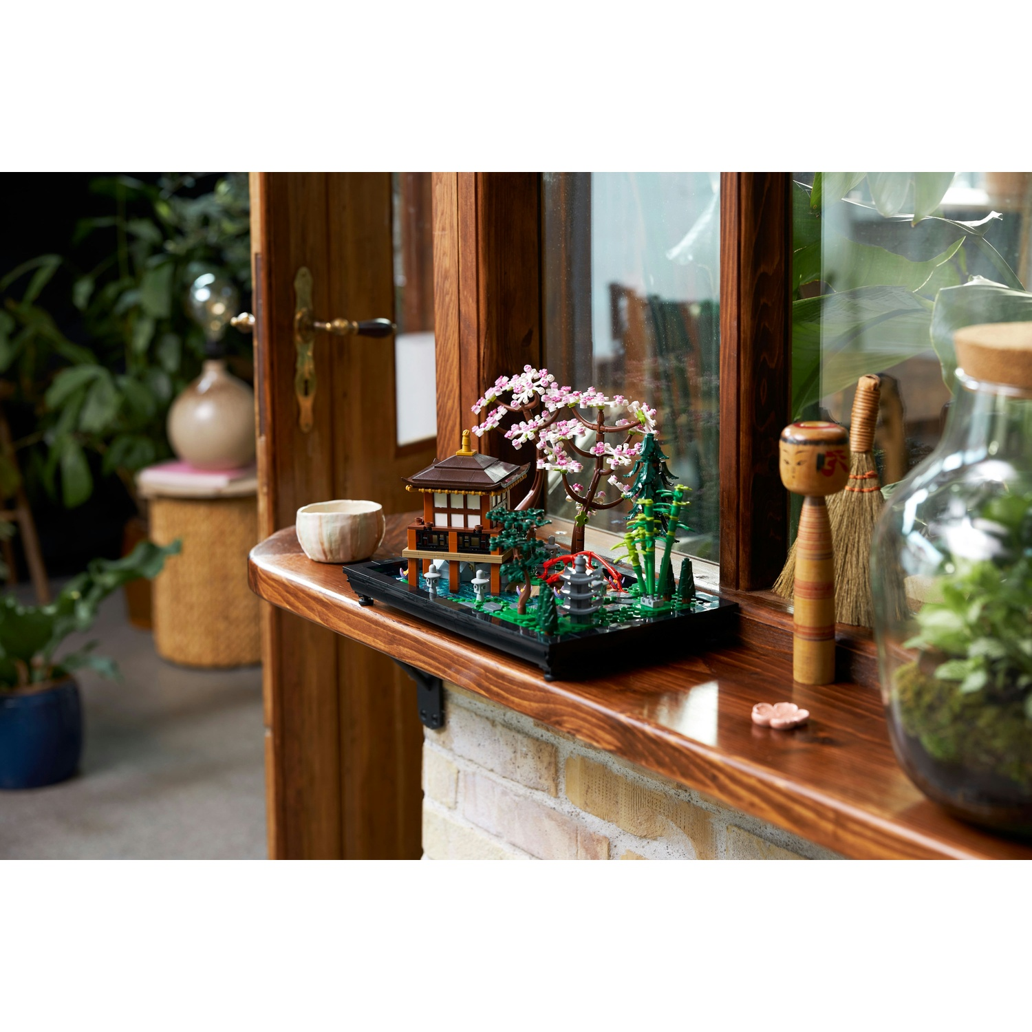 Un diorama in miniatura di un giardino giapponese è su una mensola di legno. Include una pagoda, un ponte, alberi e fiori di ciliegio.