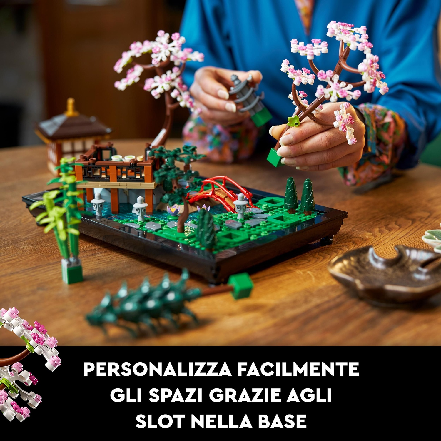 Un bonsai Lego con fiori rosa e bianchi. È su una base nera. Una persona tiene il bonsai.