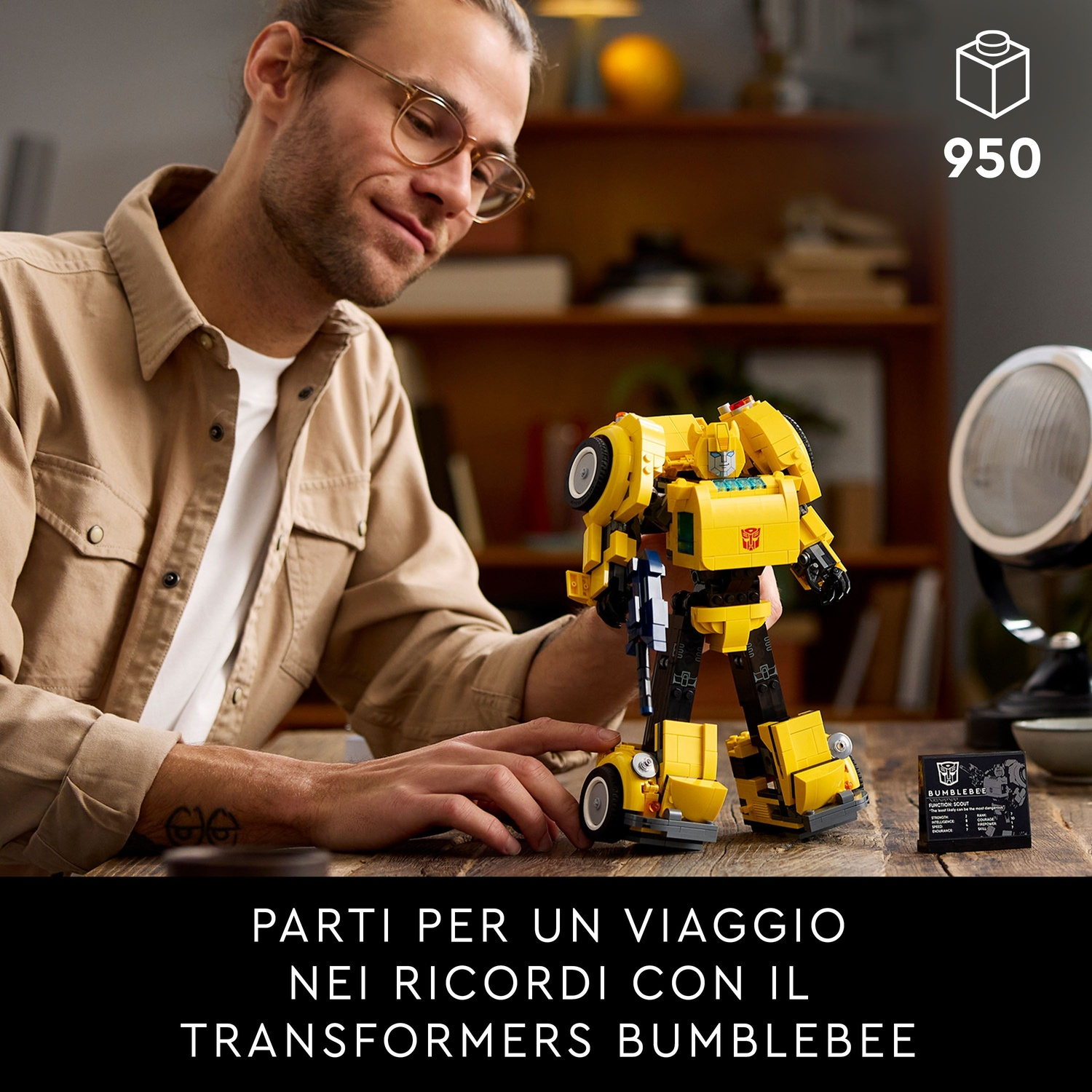 Un uomo guarda un giocattolo Transformer Bumblebee giallo. Il giocattolo è su un tavolo di legno. Testo: "Transformers Bumblebee".