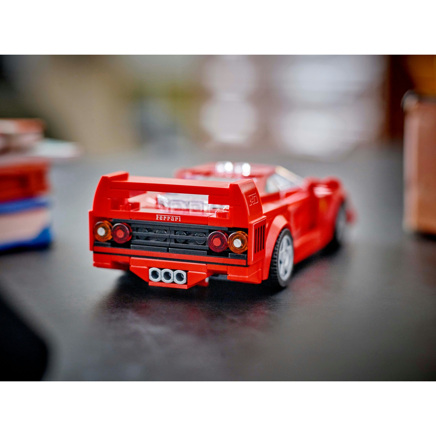 Un'auto Ferrari giocattolo rossa su una superficie scura. L'auto ha uno spoiler e tubi di scarico. Lo sfondo è sfocato.