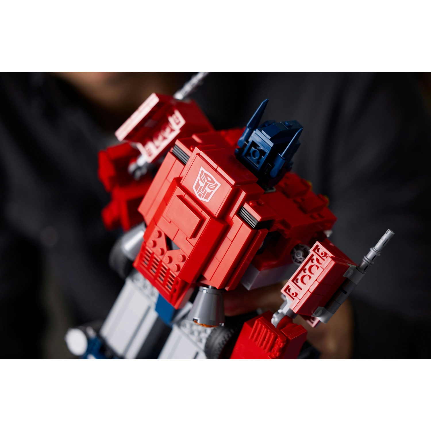 Un Transformer Lego Optimus Prime è tenuto da una persona. Il robot è principalmente rosso con dettagli blu e grigi. Lo sfondo è scuro.