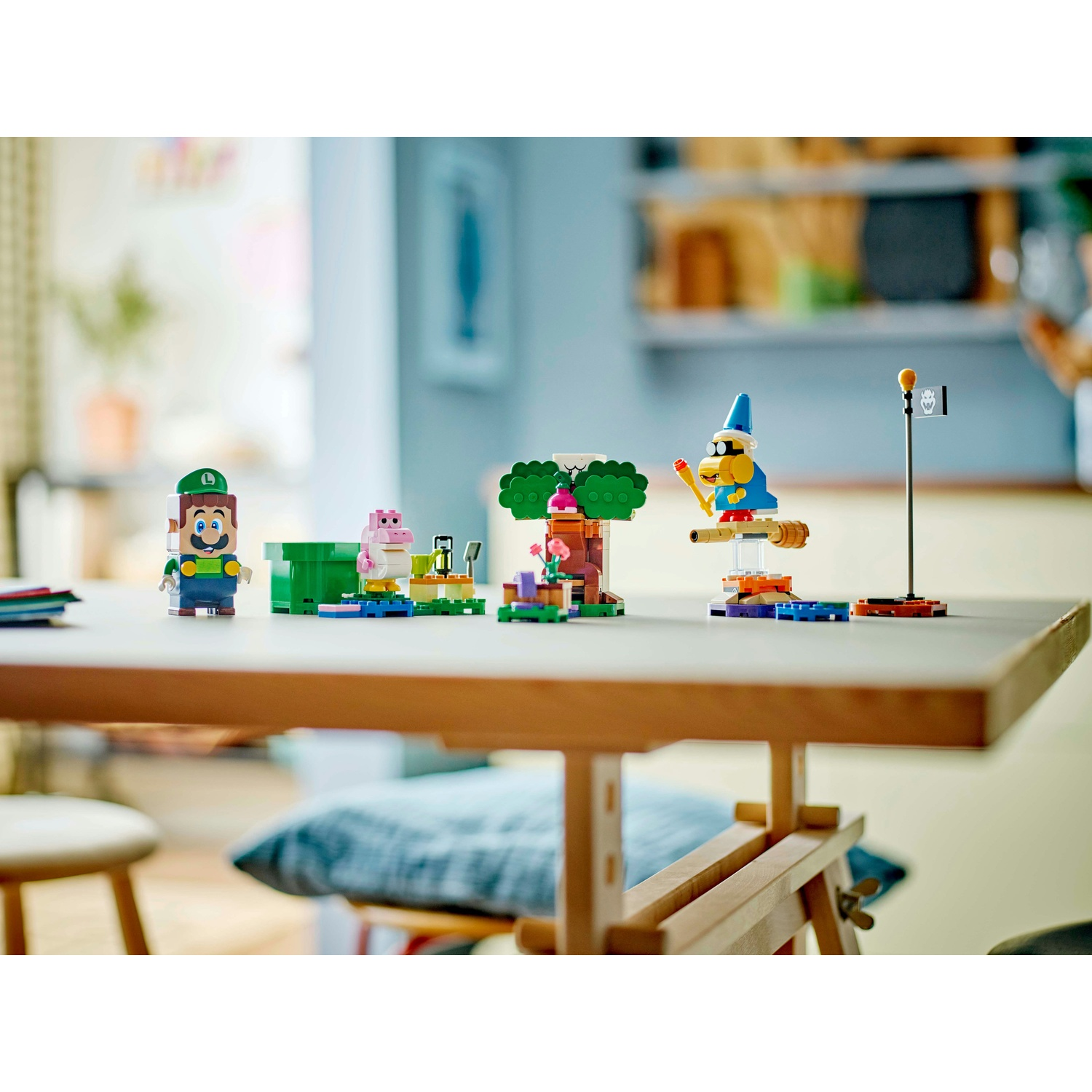 Set Lego con personaggi di Mario su un tavolo. Include Luigi, un maiale rosa, un albero e un mago su una scopa. Sfondo sfocato.