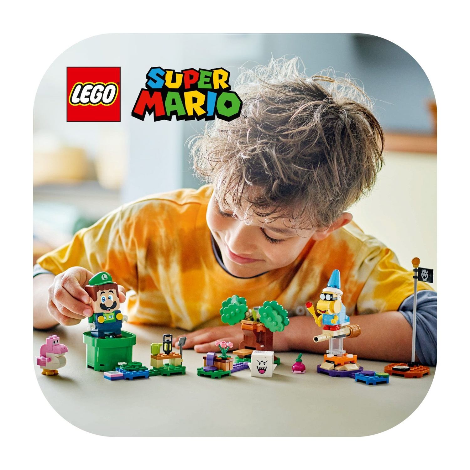 Un ragazzo gioca con Lego Super Mario. Personaggio di Luigi, altri personaggi ed elementi di scena su un tavolo.
