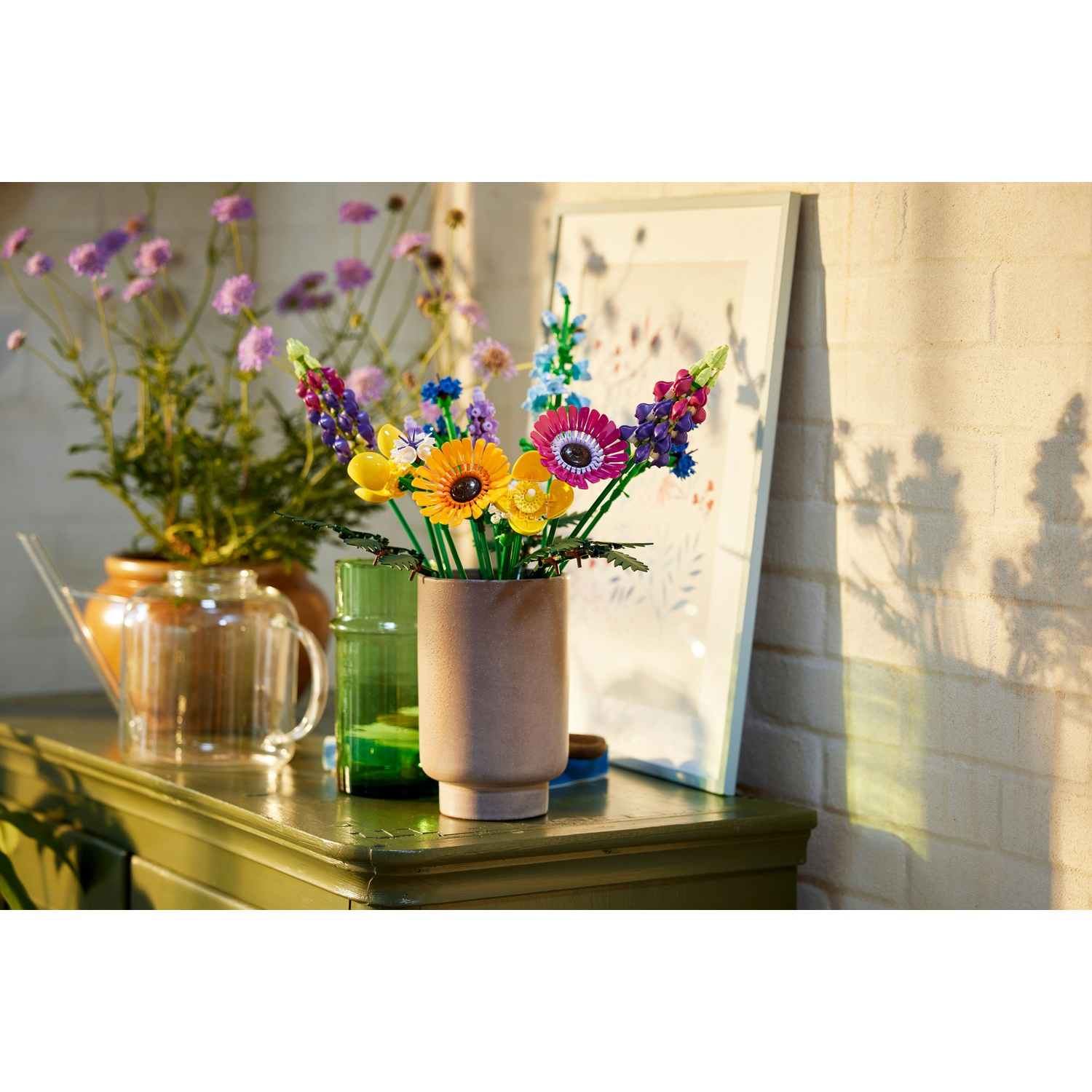 Fiori Lego colorati in un vaso su un tavolo verde, con altri vasi e un'immagine incorniciata sullo sfondo.
