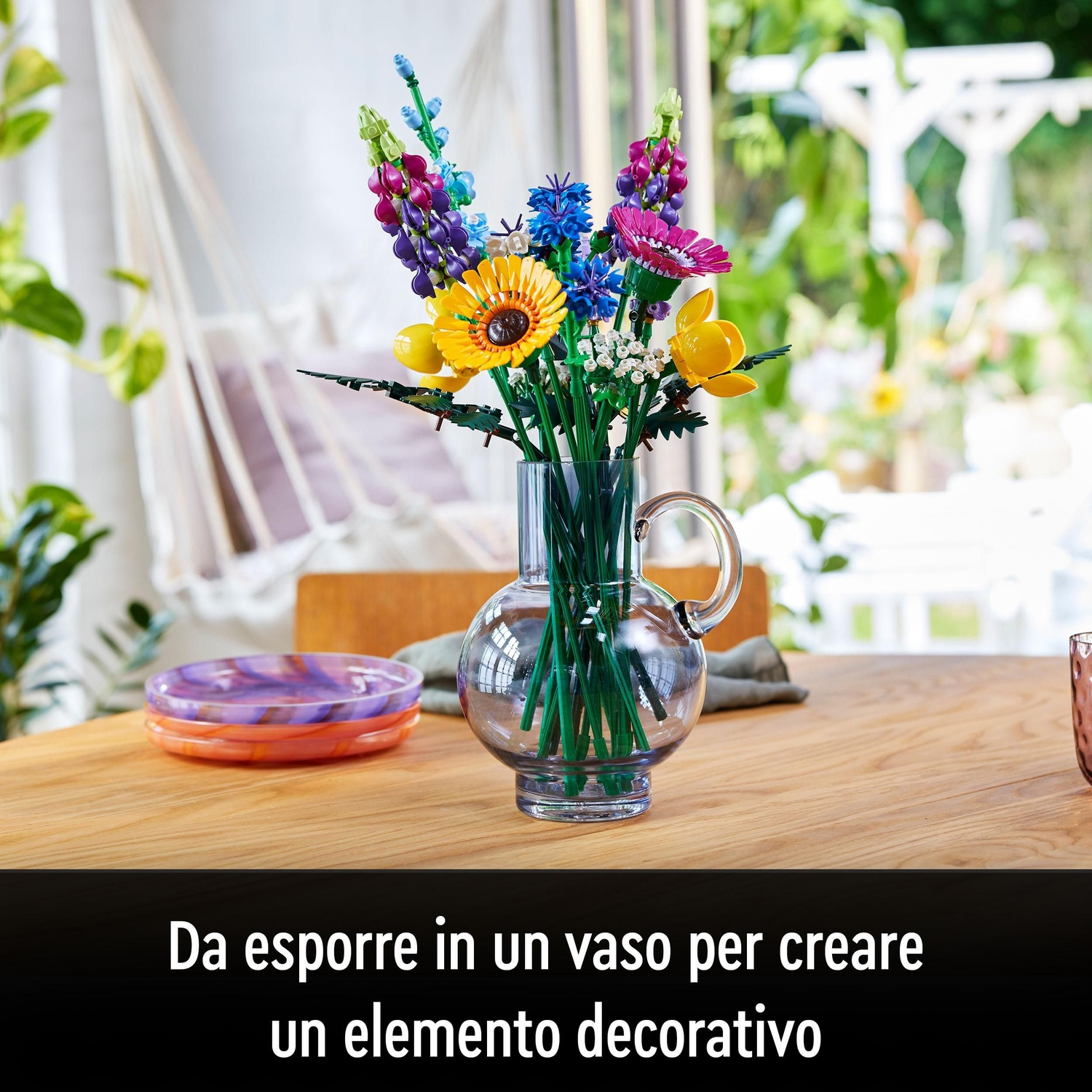 Fiori Lego colorati in un vaso di vetro su un tavolo di legno. Sfondo con altalena e vegetazione.