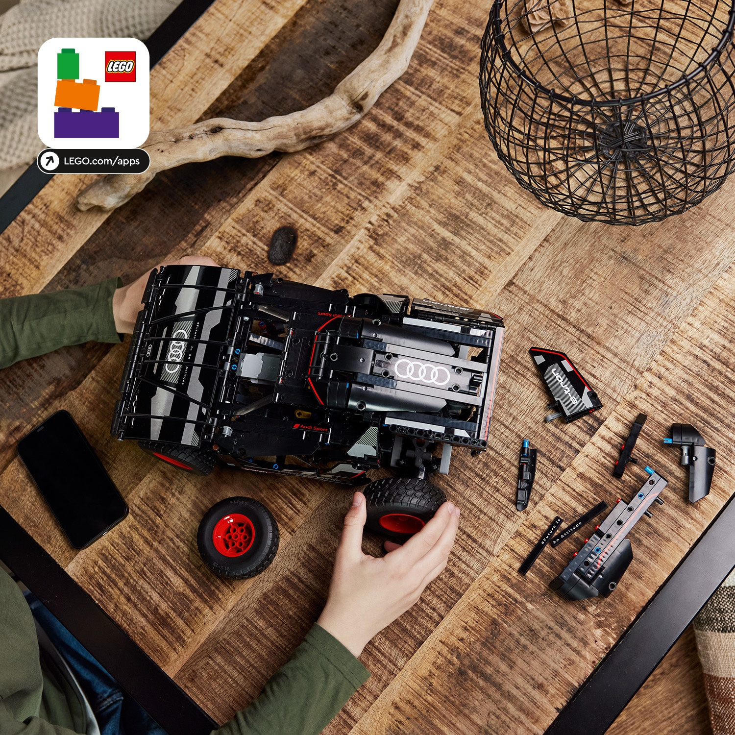 Un'auto Lego Audi viene assemblata su un tavolo di legno. Parti e un telefono sono accanto. Le mani stanno costruendo l'auto.