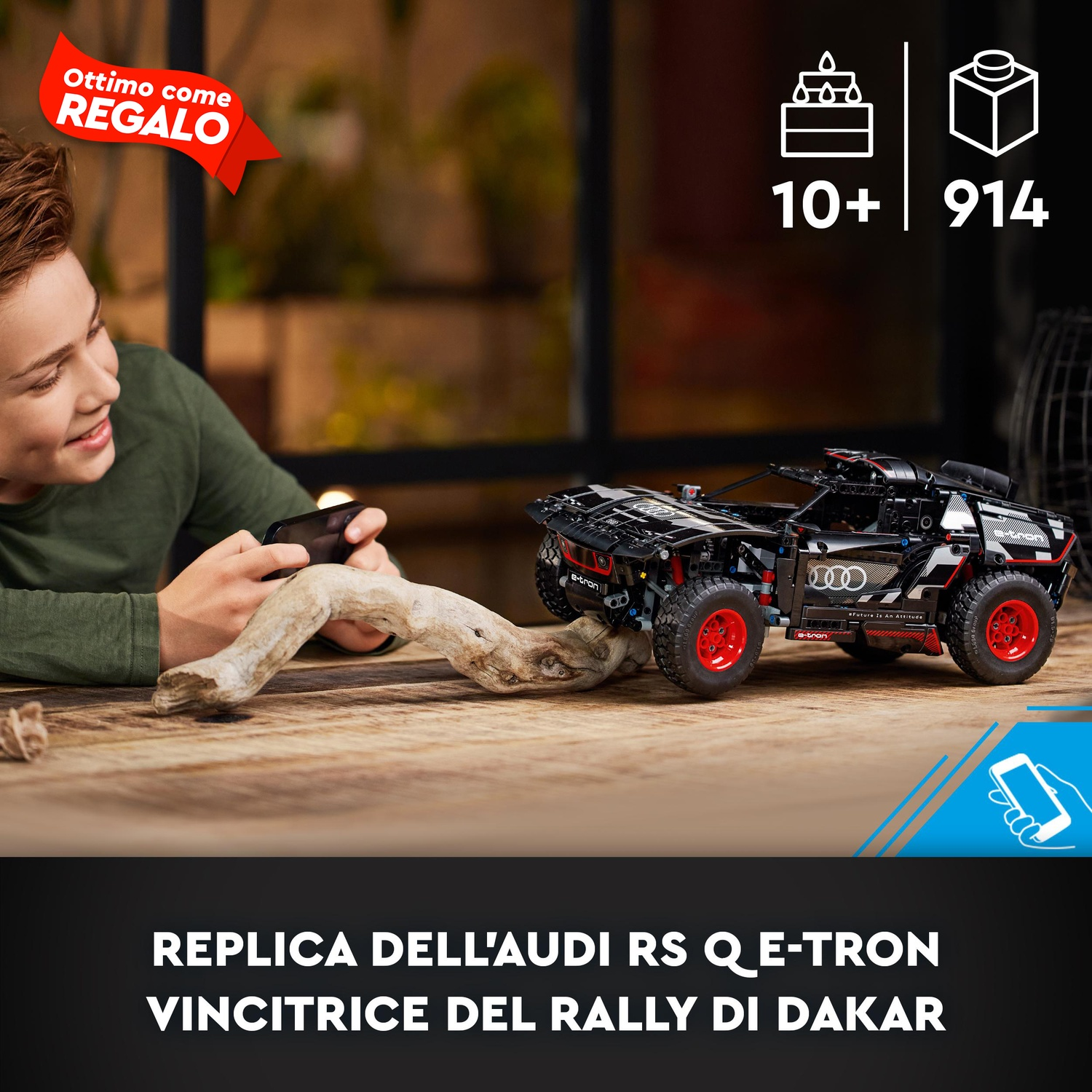 Un ragazzo guarda un modello Lego Audi RS Q e-tron. Il modello è nero con ruote rosse. Il testo dice che è un buon regalo.