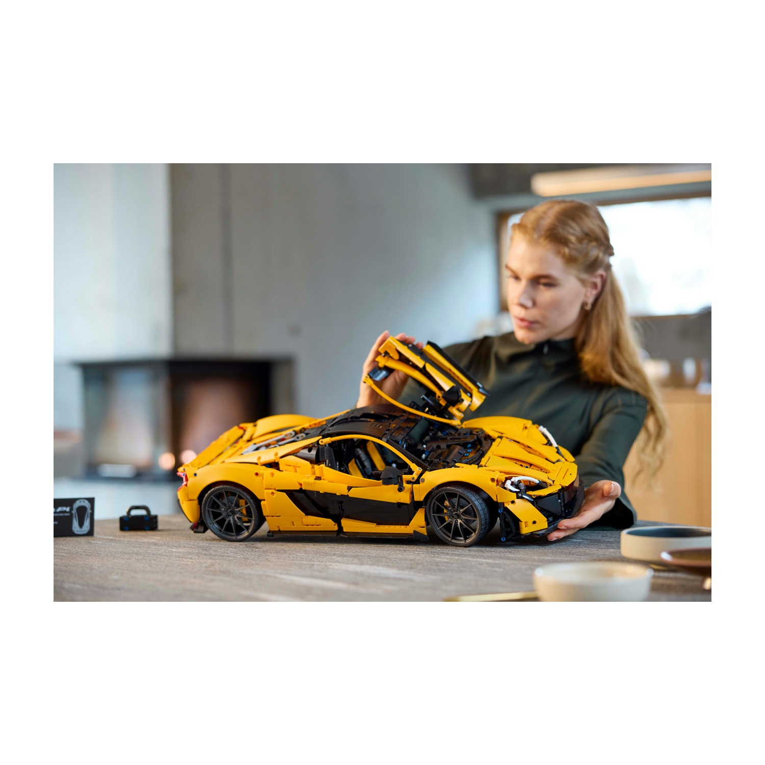 Una donna assembla un'auto sportiva Lego gialla e nera. L'auto è su un tavolo. La donna tiene in mano un pezzo dell'auto.