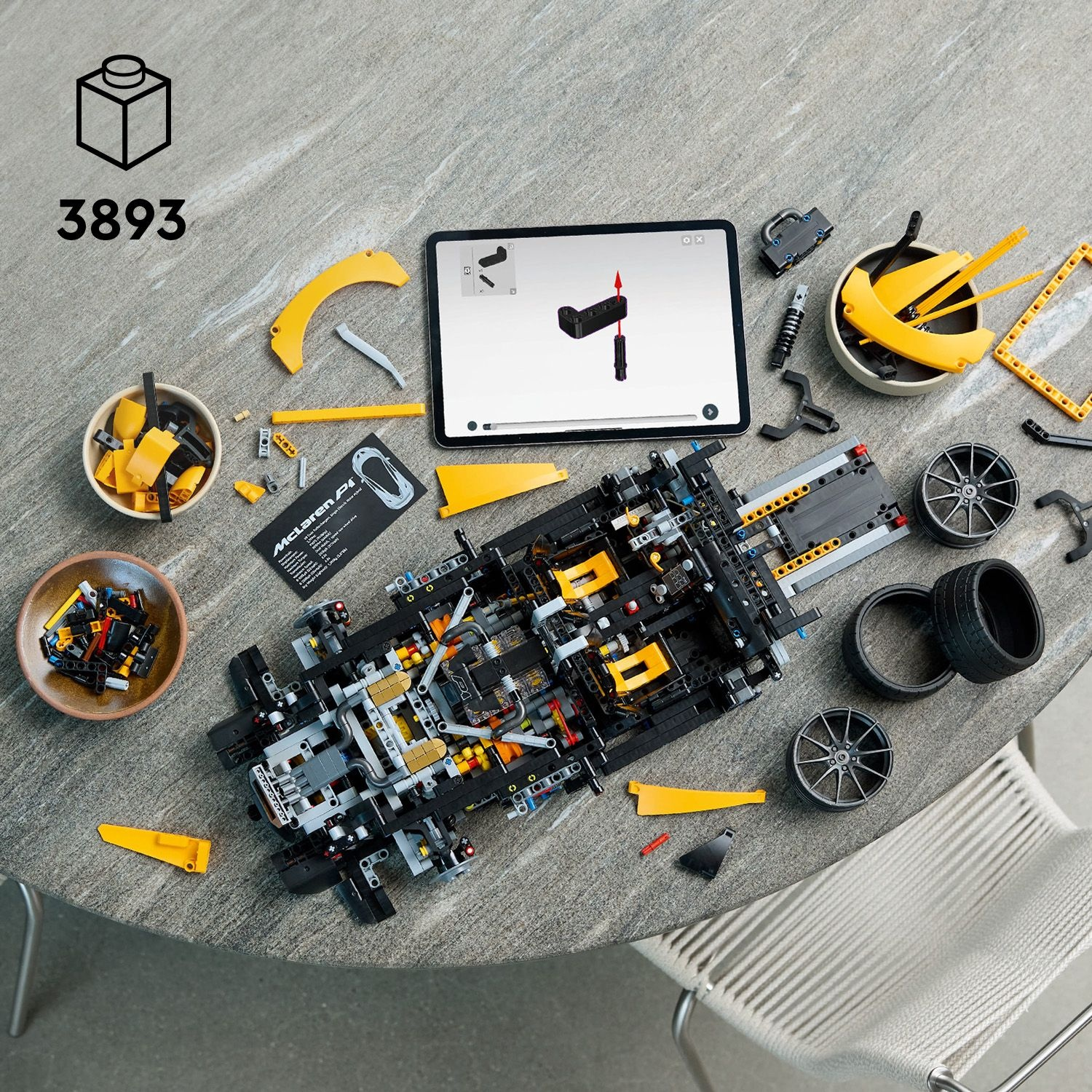 Parti di auto Lego disposte su un tavolo. Un tablet mostra le istruzioni. Ruote, pneumatici e altri componenti sparsi.