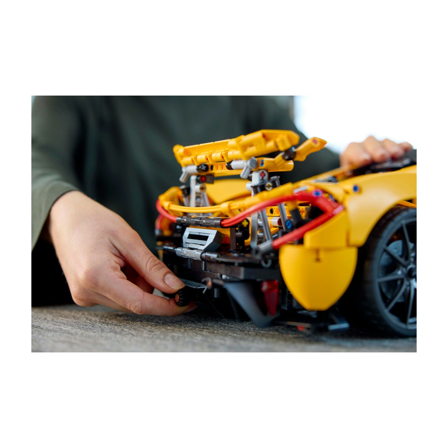 Una persona assembla un modello di auto sportiva Lego giallo. Le mani regolano un componente nero posteriore. L'auto è su una superficie grigia.