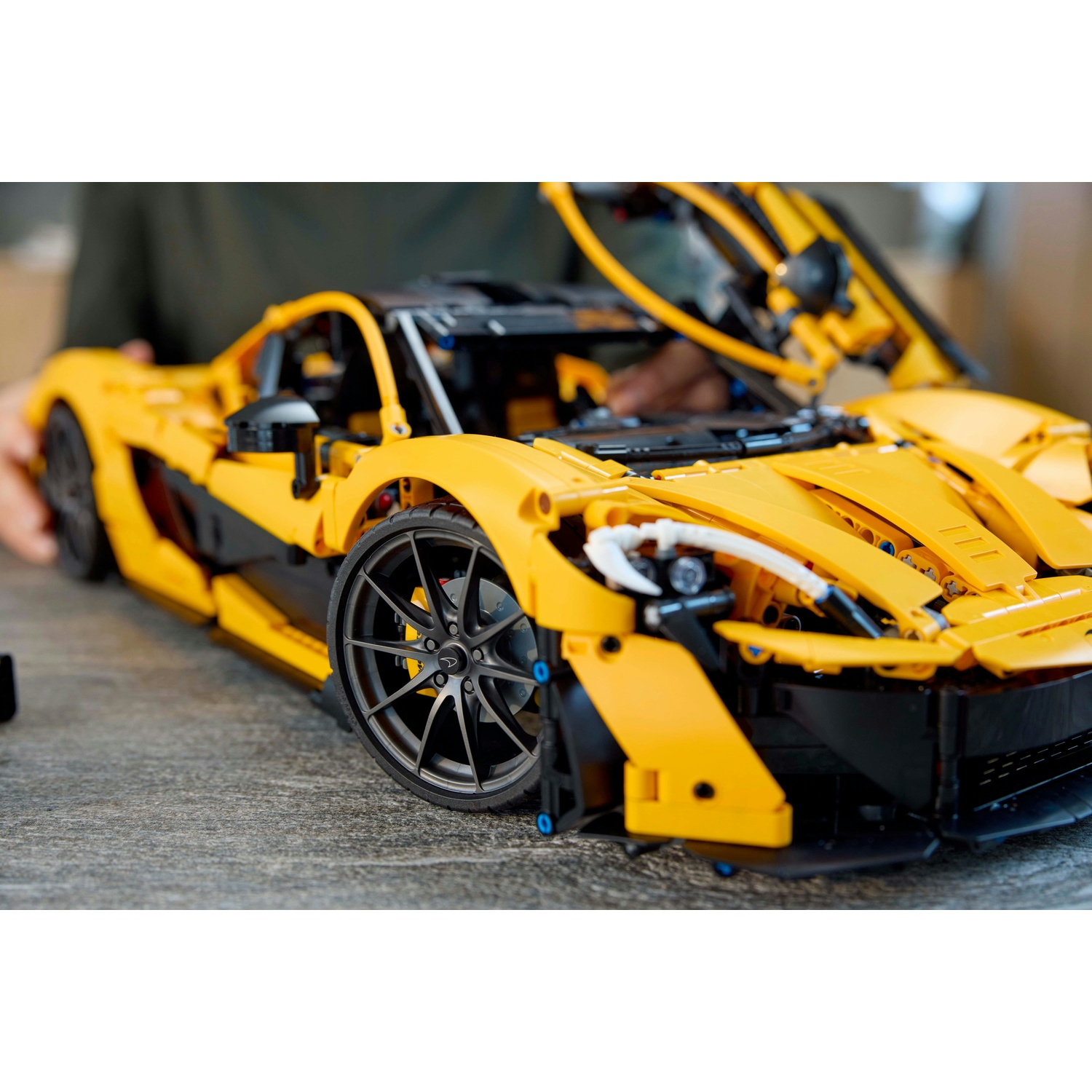 Un'auto sportiva Lego gialla su una superficie grigia, con la portiera aperta. Le ruote sono nere, mani visibili.