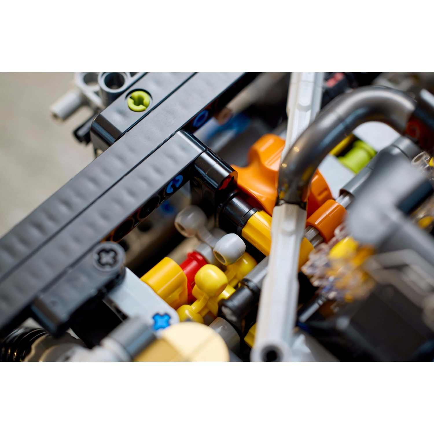 Primo piano di parti Lego Technic. Sono assemblati pezzi neri, gialli, arancioni e grigi. È visibile anche un tubo metallico curvo.