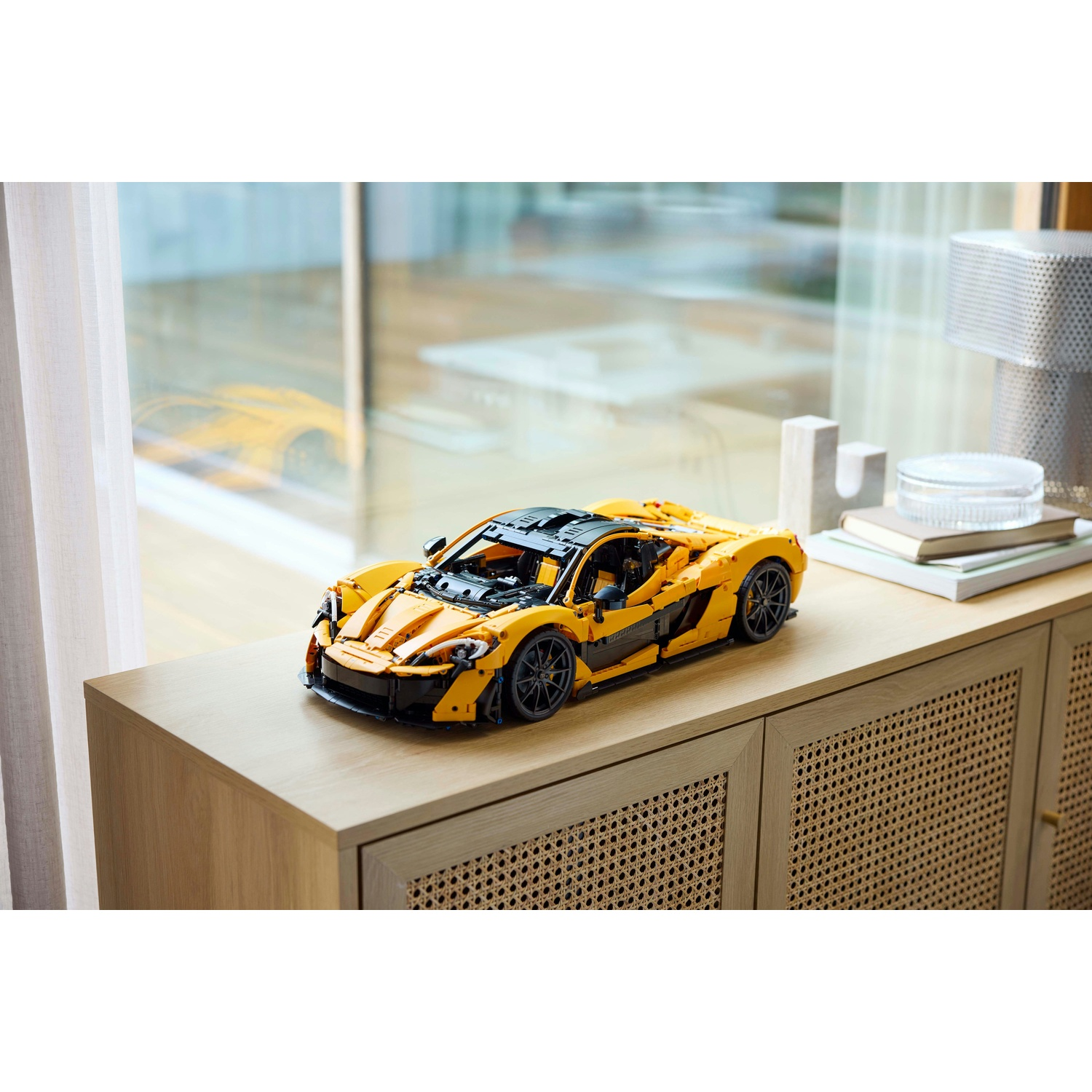 Un'auto sportiva Lego gialla è appoggiata su un mobile di legno, di fronte a una finestra. Altri oggetti sono sul mobile.
