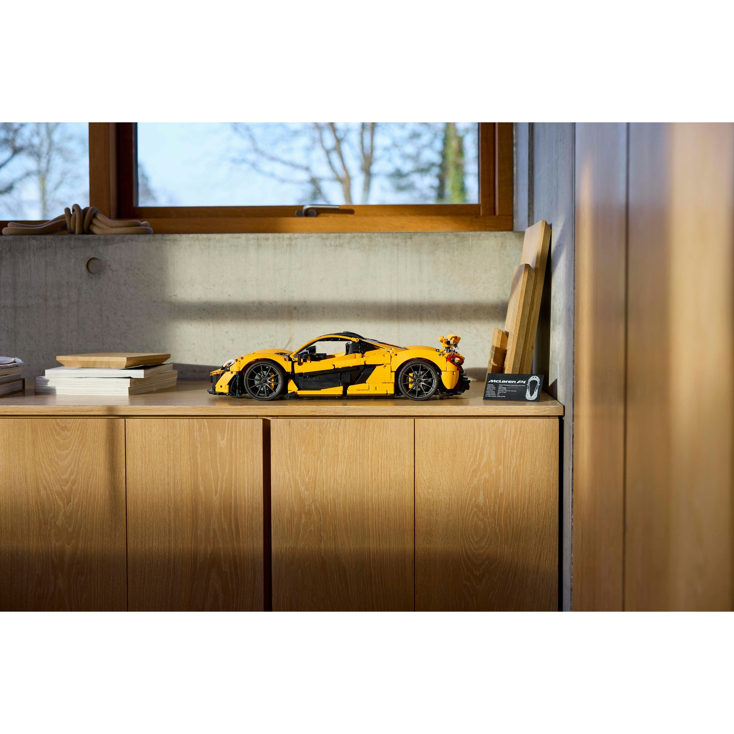 Un modello di auto Lego McLaren F1 giallo è su un mobile in legno. Una finestra e pannelli di legno sullo sfondo.